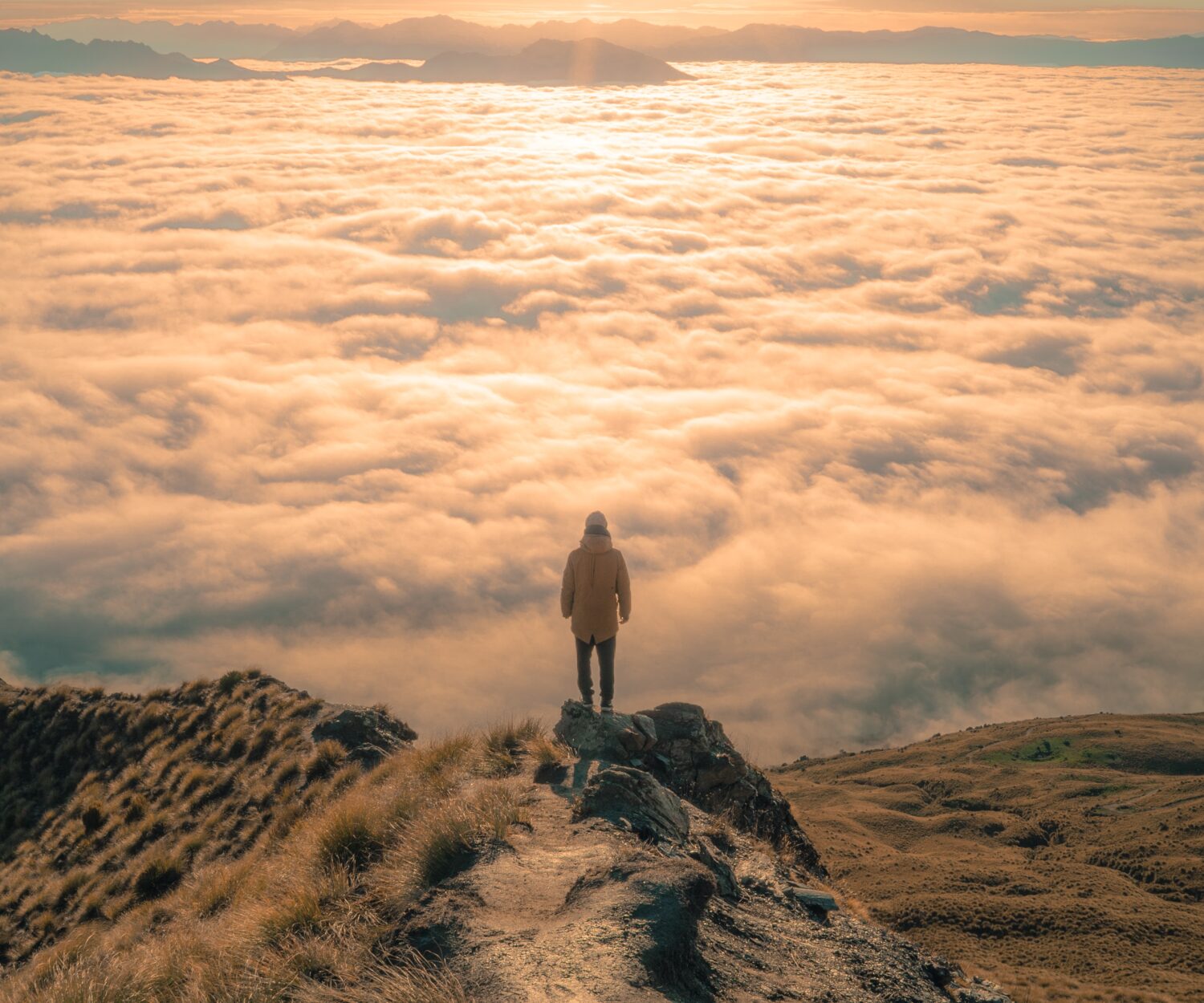 Ein Mann steht auf einem Berg schaut auf ein Wolkenmeer im Sonnenschein