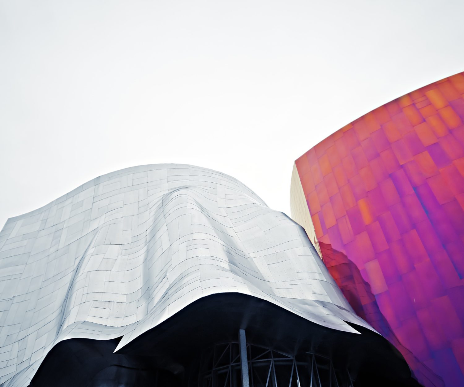 Moderne Gebäude, links in silber, rechts bunt vor einem weißen Himmel.
