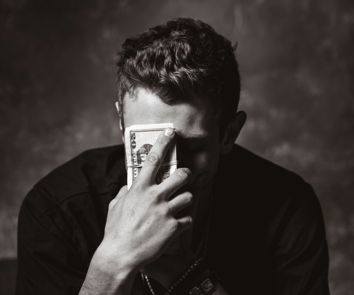 Ein Mann hält sich Pokerkarten vor das Gesicht. Das Motiv ist Schwarz & Weiß