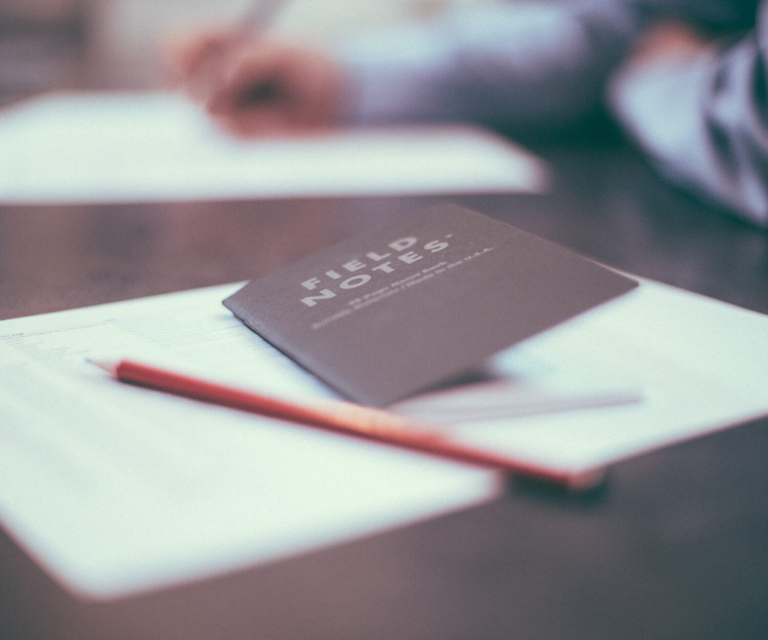 Portraitaufnahme eines Notebooks mit Stift auf einem Tisch. Darum ein Unschärfeeffekt