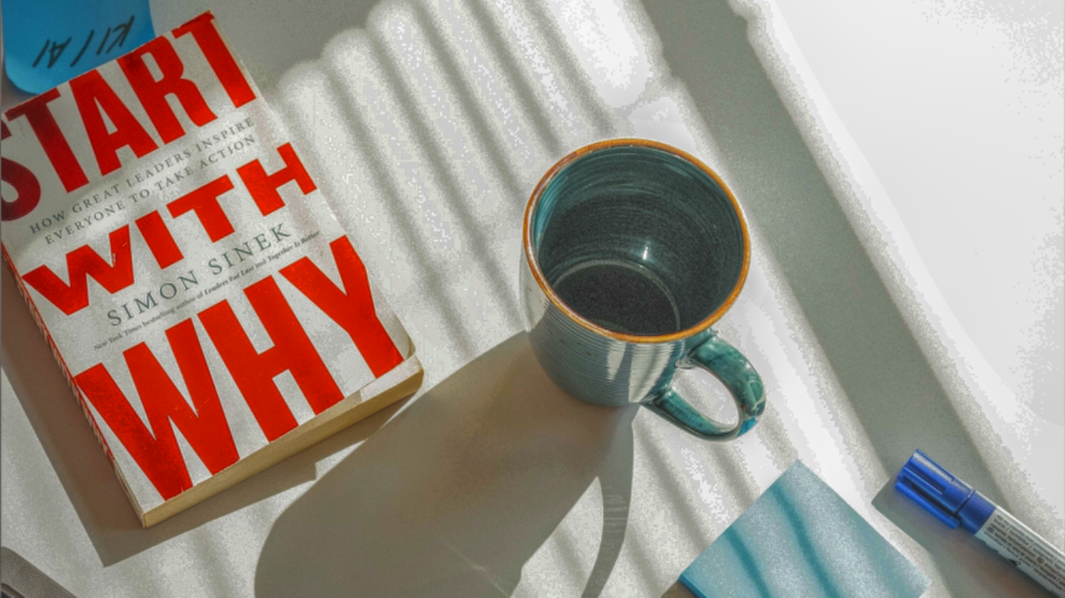 Ausschnitt Arbeitsplatz im Büro von Fuchs Devils Wild mit Kaffetasse, Laptop im Anschnitt, Stift, Post-its blau und dem Buch Start with Why von Simon Sinek